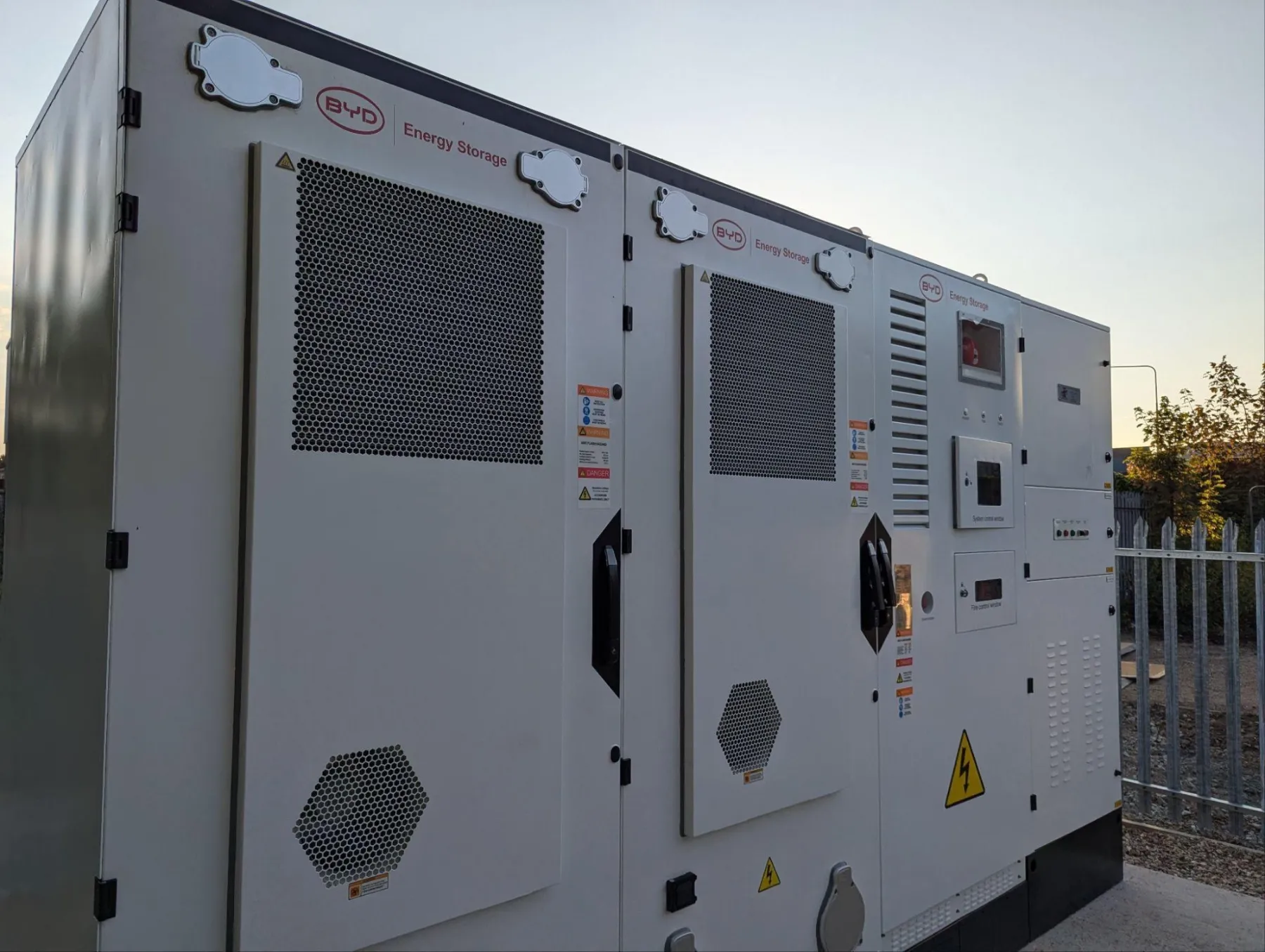 Two BYD battery cabinets and a control cabinet at golden hour behind a palisade fence